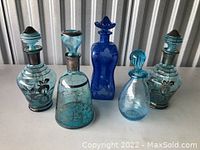 Five vintage blue glass decanters of varying shapes and sizes arranged in a row, showing overall lot contents.
