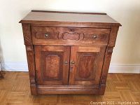 Front view of brown wooden cabinet with one drawer and double doors, showing metal handles and keyholes.