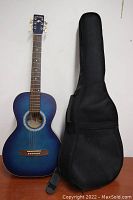 Full front view of blue acoustic guitar and black soft case side by side