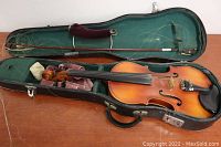 View of violin in open hard case, showing violin body, bow placed inside case, and some loose strings.