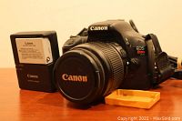 Canon EOS Rebel T2i DSLR camera body with lens attached, battery charger, and yellow power adapter on wood table.