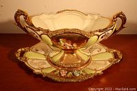 Full view of the porcelain candy dish sitting on the matching oval platter showing cream and pastel green colors with gold and floral accents.
