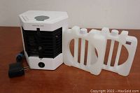 Full view of the Arctic Air desktop air conditioner showing front louvers, water tanks, and charger on wood surface.