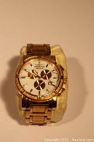Front view of Invicta gold tone wristwatch on a cushion displaying white dial with three chronograph sub-dials and gold tone bezel.