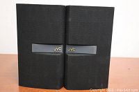 Front view of two JVC speakers with cloth covered fronts and JVC logo on each.