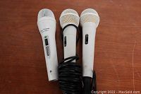 Three wired karaoke microphones on a wooden surface, showing overall fair exterior conditions.