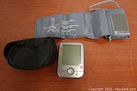Full view of digital blood pressure monitor, cuff, and carry case on a wooden surface
