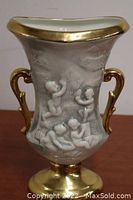 Full view of the ceramic vase showing gold handles, base, and rim with cherub relief sculpture on front.