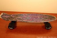 Side view of the Penny skateboard showing the electrical storm graphic deck design and two intact wheels; one wheel is missing on the other side.