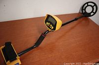 Full view of the metal detector showing the control box, handle, shaft, and circular search coil on a wood surface.