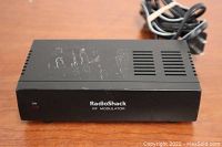Front view of black rectangular RadioShack RF modulator with power cord showing RadioShack branding and On indicator light.