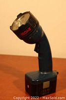 Side view of blue Ryobi flashlight showing pistol grip handle and rechargeable battery pack at base.