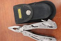 Photo showing the Stanley multi-tool partially unfolded next to its black nylon carrying case with snap button closure.