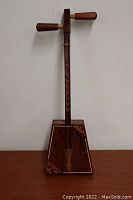 Full view of wooden stringed instrument showing trapezoidal resonator body, two strings, and wooden tuning pegs.