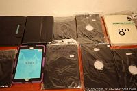 Multiple various black tablet cases with packaging, includes iPad Mini 4 case with purple and black protective cover and Samsung T380/385 case