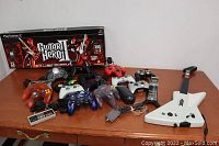 Wide shot showing all video game controllers and Guitar Hero guitars on a wooden table.