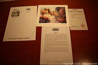 Photo of paperwork including artist info, certificate of authenticity and packaging envelope with artist and artwork info.