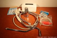 Lot items arranged on a surface including silver faucet spout, handheld shower head with hose, white tissue box cover, flexible hose with red bulb pump, small hardware packs and set of white hooks.