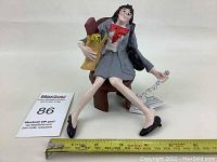 Front and left side view of a seated woman figurine holding a telephone handset and a paper bag, showing size and details.