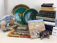 Lot overview showing decorative plates, books, metal boxes, and soft seder set toy