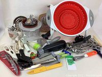 Photo displaying collage of many utensils including knives, scissors, peelers, and a collapsible red silicone colander.