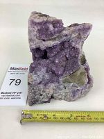 Front view of raw amethyst crystal geode showing the purple crystals and rough stone matrix, with a tape measure indicating approximately 6 inches height.