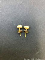 Pair of small stud earrings with irregular freshwater pearls set on 14K gold posts on a dark fabric background.