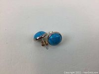 Pair of blue oval stone stud earrings showing one sterling silver backing and one 14K gold backing, placed on white background.
