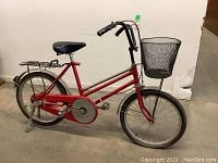 Side profile of the red vintage youth bike showing convertible frame, front wire basket, black saddle, rear rack, and deflated tires.