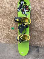 Green youth-sized Burton snowboard with yellow and black bindings attached, showing signs of wear on bindings and board surface.