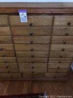 Full front view of oak apothecary cabinet showing all 27 drawers and knobs