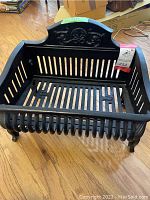 Full angled view of the black cast iron fireplace stand sitting on hardwood floor showing front, sides, and top details.