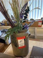 Large gray ceramic crock filled with artificial tall grasses and purple flowers, showing front with label and detail of blue decoration