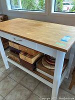 Full view of kitchen island showing butcher block top, white frame, drawer, bottom slatted shelf