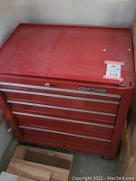 Full view of red Craftsman metal tool box on caster wheels, showing front and top surfaces with some scratches and wear.
