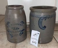 Two grey salt-glazed stoneware crocks side by side on tile floor
