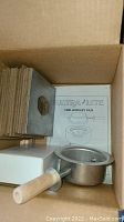 Box interior showing instruction manual, metal crucible pot with handle, fiber boards stack