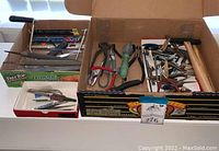 Overview photo showing multiple cardboard boxes containing various jewelry making tools such as pliers, files, cutters, and hammers.