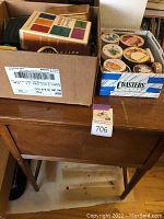 Wood cabinet surface with boxes of sewing notions including thread spools and coasters