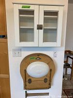 White wall cabinet with mesh screen doors and metal lock mounted on wall, above mounted marine sink with porcelain bowl and wooden backing, brass towel bar attached below the sink