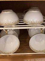 Four upside-down tea cups with gold handles and gilt border on rack