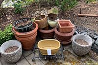 Photo showing multiple planter pots stacked and arranged on patio stone with dirt inside, including the yellow plastic planter and textured stone pots, plus a small white planter shaped like a birdhouse