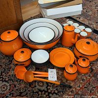 Overview of lot showing all items: mixing bowls, enamel pots, serving spoons, plates, cups, and bowls in orange and white enamel.