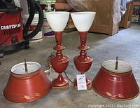 Two assembled red table lamps flanked by two red metal shades on concrete floor.