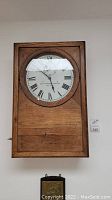 Front view of oak-cased wall clock showing white dial with Roman numerals behind glass