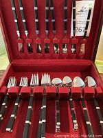 Open red velvet lined storage case displaying full flatware set arranged by type