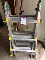 Steel folding ladder seen from front, showing yellow safety grips on steps and locking mechanism on sides.