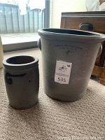 Two stoneware crocks on carpet near a window. Larger crock with blue ink stamp 'BANGOR STONEWARE CO BANGOR MAINE 4', smaller pot with cobalt swirl decoration visible.