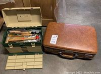 Photo showing open Plano toolbox filled with assorted jewelry making tools next to closed camel colored suitcase