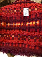 Close up of red and burgundy checkered wool rug with looped fringe trim and auction tag